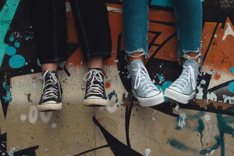 Image shows two young people's legs dangling from a skate park ramp whilst they hang out together. 